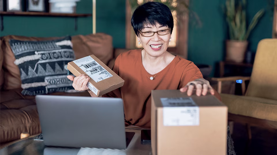 Mature woman looking at packages on desk with laptop open